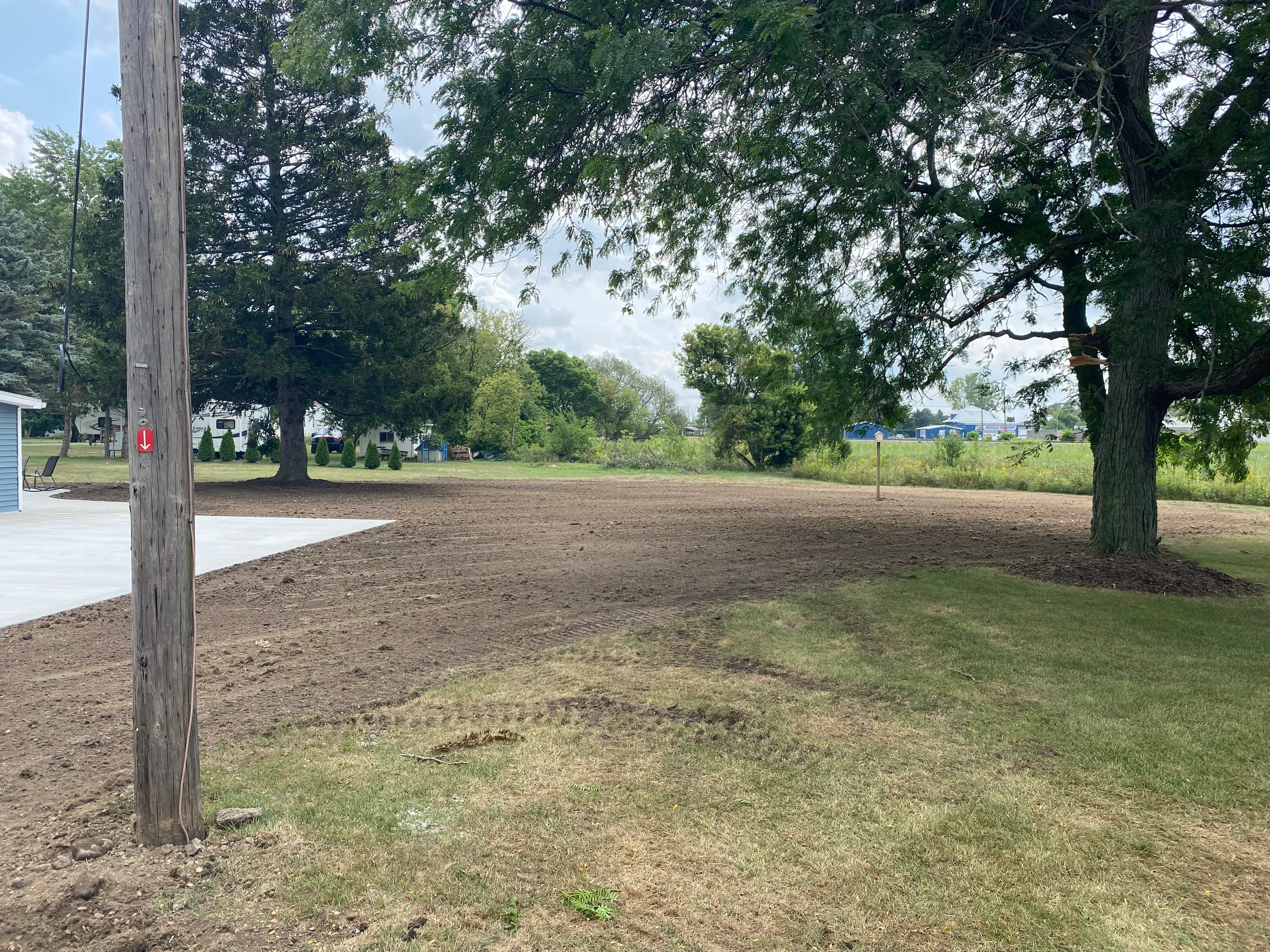Graded dirt lot with mature trees, compacted soil base, and cleared site preparation work
