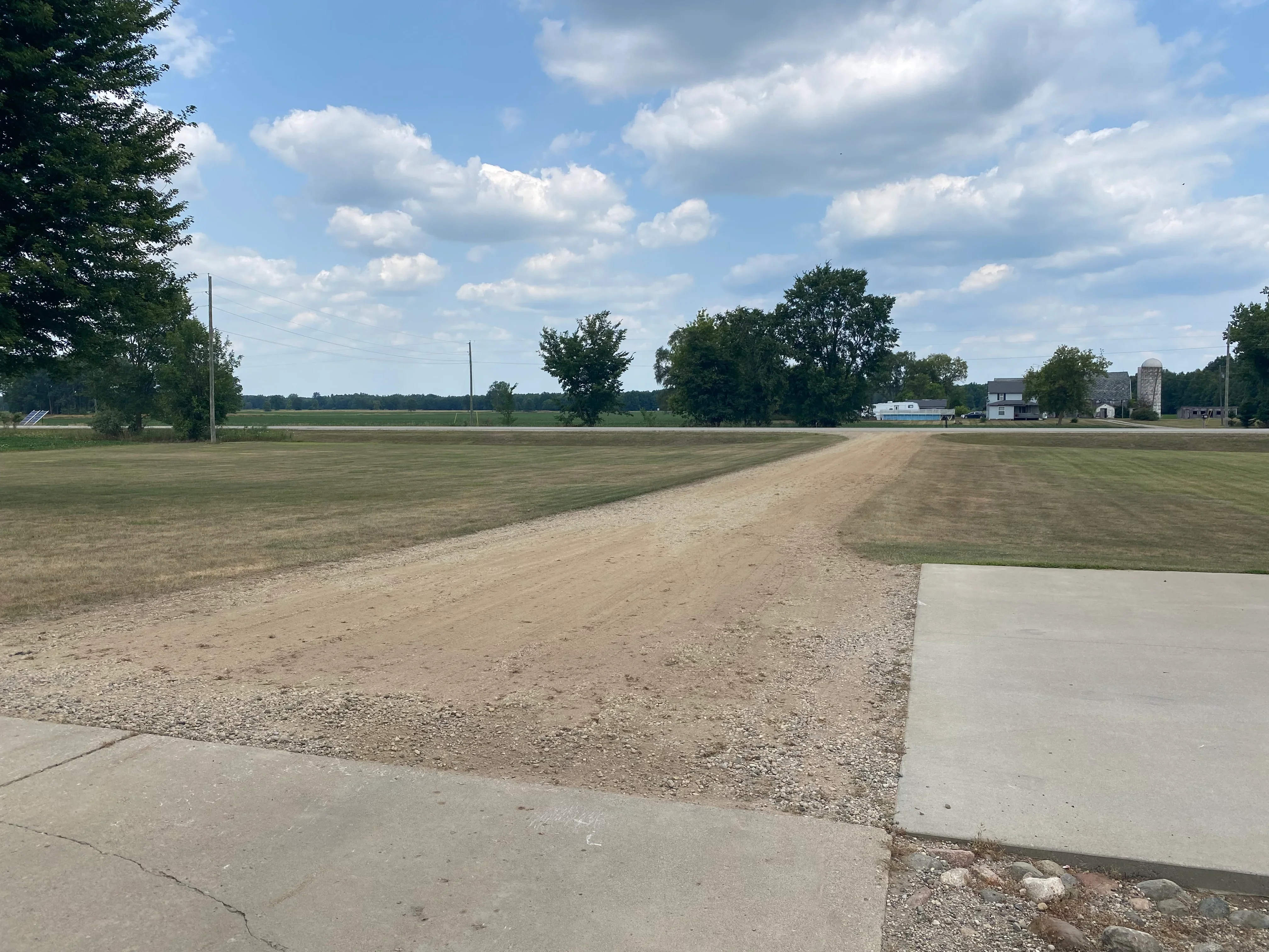 Gravel driveway with concrete apron on rural property with open fields