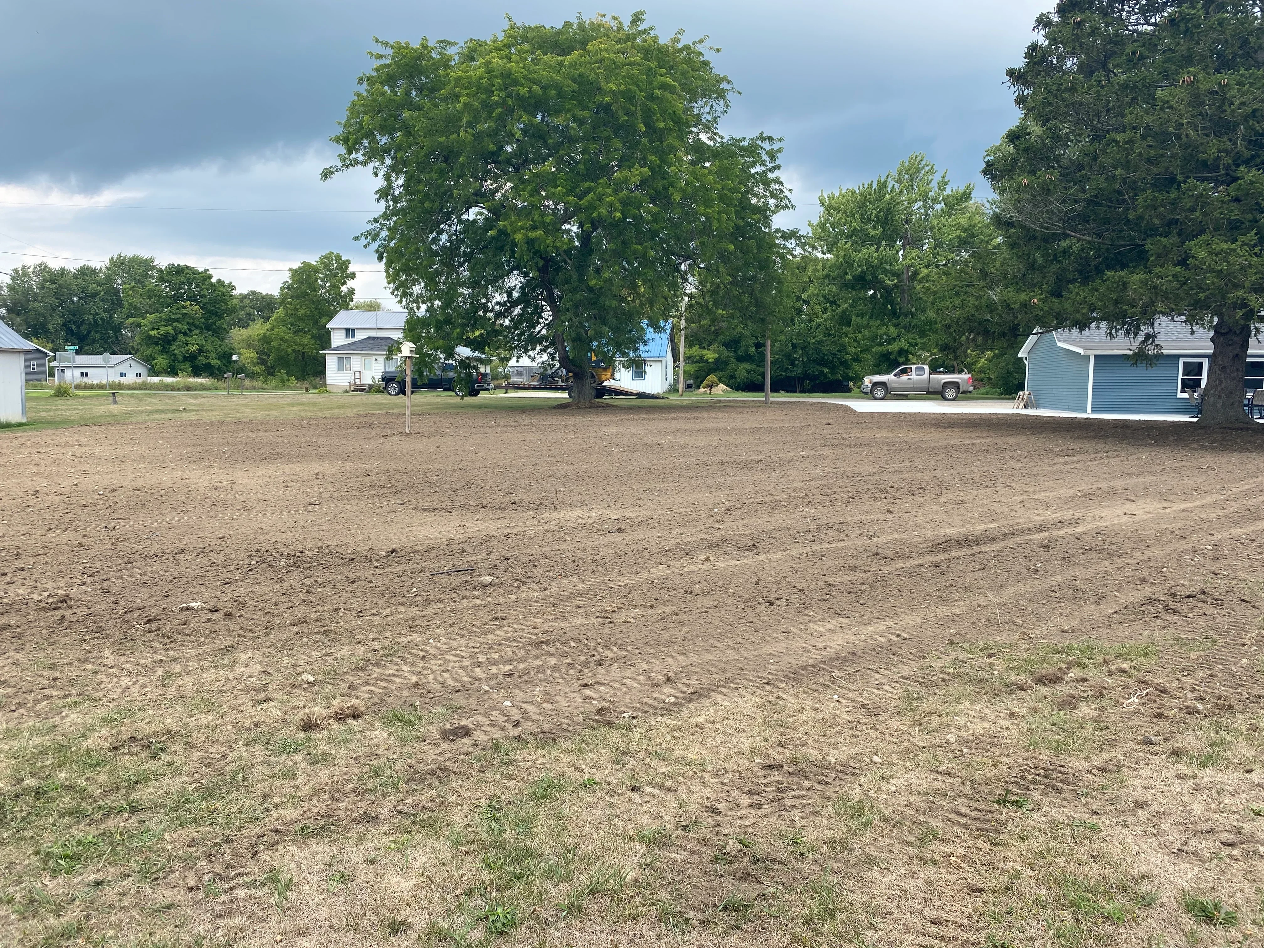 Graded residential lot with compacted soil and cleared earth, mature trees at property edges