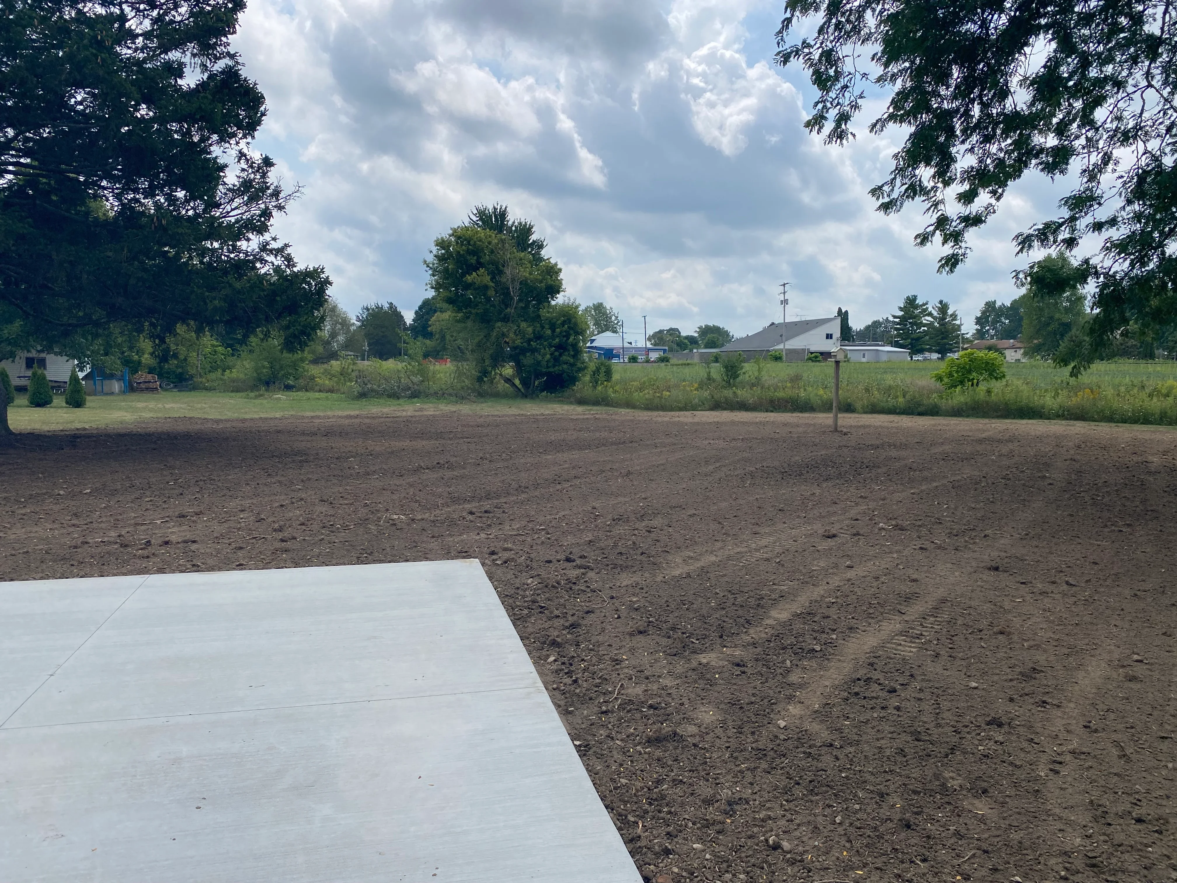 Newly poured concrete driveway pad with compacted soil base on rural property